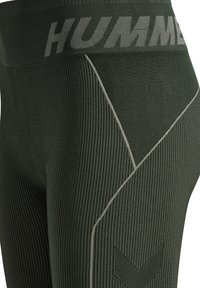 Mörkgröna leggings med ribbad textur, med ett grått logoband i midjan och diagonala sömmar för extra detaljer.