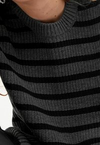 Pull en maille avec un col rond, base grise à rayures horizontales noires, tissu texturé et poignets côtelés pour plus de détails.