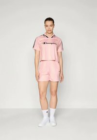 Roosa spordikomplekt, mis sisaldab lühikeste varrukatega särki mustade detailide ja logo ehk riidekomplekt. Sile materjal, mis tagab mugava istuvuse.