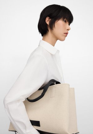 Beige Tragetasche mit einem Körper aus strukturiertem Stoff und schwarzen Ledergriffen. Verfügt über ein strukturiertes Design und minimalistische Hardware-Akzente.