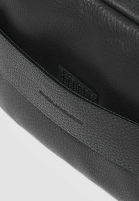 Borsa in pelle nera con superficie texturizzata, cuciture sobrie e etichetta del marchio. All'interno presenta una fodera morbida e un design minimalista.