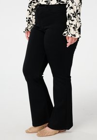 Zwarte flared jeans met een gladde textuur en een klassiek vijf-pocket ontwerp. Gepaard met lichtgekleurde, geperforeerde ballerina's en een patroon top.