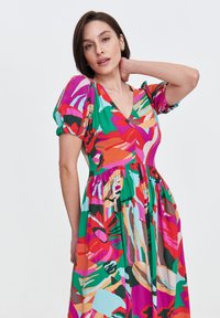 Kolorowa sukienka w kwiaty z dekoltem w kształcie litery V, bufiastymi rękawami i marszczoną talią. Wykonana z lekkiego materiału w odcieniach zieleni, różu i pomarańczu.