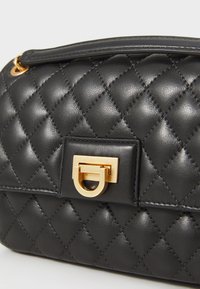 Black quilted leather handbag with a gold hardware clasp, featuring a structured shape and smooth texture. Accented by a top handle.