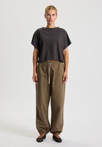 Maglietta grigia oversize a maniche corte con orlo arrotondato, abbinata a pantaloni khaki larghi con vita elasticizzata e coulisse. Scarpe basse nere intrecciate.