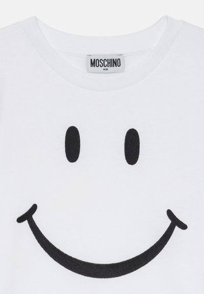 Bílé dětské tričko s velkým černým vyšívaným úsměvem a štítkem značky Moschino uvnitř límečku.