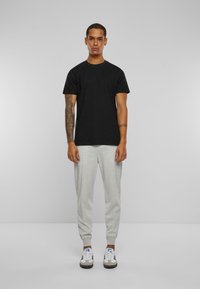 Zwarte katoenen t-shirt met korte mouwen, gecombineerd met lichtgrijze, tapered broek. De outfit wordt compleet gemaakt met witte sneakers met donkere accenten.