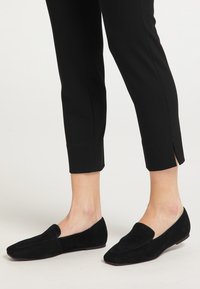 Loafers negri din suede, cu vârf ascuțit, talpă plat�ă și design slip-on, asortați cu pantaloni negri croiți, cu.spacing lateral.