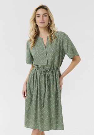 Polka dot dress in olive green, short sleeves, buttoned front, drawstring waist, knee-length, lightweight fabric with smooth texture.