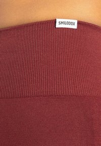 Burgundy randig tyg med en texturerad midjeband; har en vit etikett märkt "SMILODOX" vid den övre kanten.