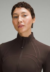 Brun atletisk top med høj krave, lynlås lukning og kontrasterende syninger. Glat, strækbart stof med en tætsiddende pasform.
