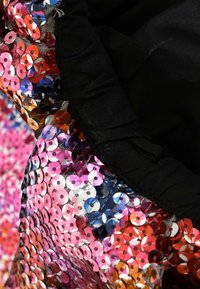 Gros plan de sequins brillants multicolores recouvrant densément un tissu à côté d’un tissu noir uni avec des bords froncés et une boucle en tissu.
