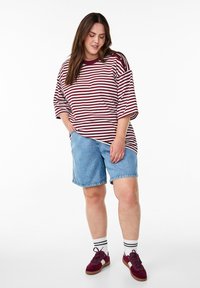 Röd- och vitrandig, löst sittande skjorta med korta ärmar, paired med blå denimshorts. Outfitten kompletteras av vinröda sneakers och randiga strumpor.