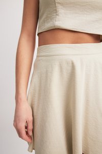 Set de top scurt și fustă de culoare bej deschis, realizat dintr-un material texturat. Fusta are un tiv neted și o siluetă fluidă.