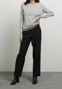 Grijze sweatshirt met lange mouwen en ribbels bij de kraag en manchetten, gecombineerd met zwarte wijde broek. Model draagt zwarte enkellaarsjes met hak.