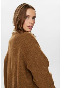 Vêtement en mélange de laine marron avec une coupe décontractée et un col châle, présentant une surface texturée et un design à épaules tombantes.