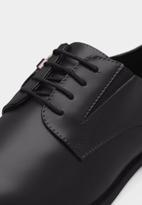 Μαύρο δερμάτινο παπούτσι με κλειστό κορδόνι, λείο φινίρισμα και καθαρά ραφές κοντά στις τρύπες για τα κορδόνια και στα πλάγια.