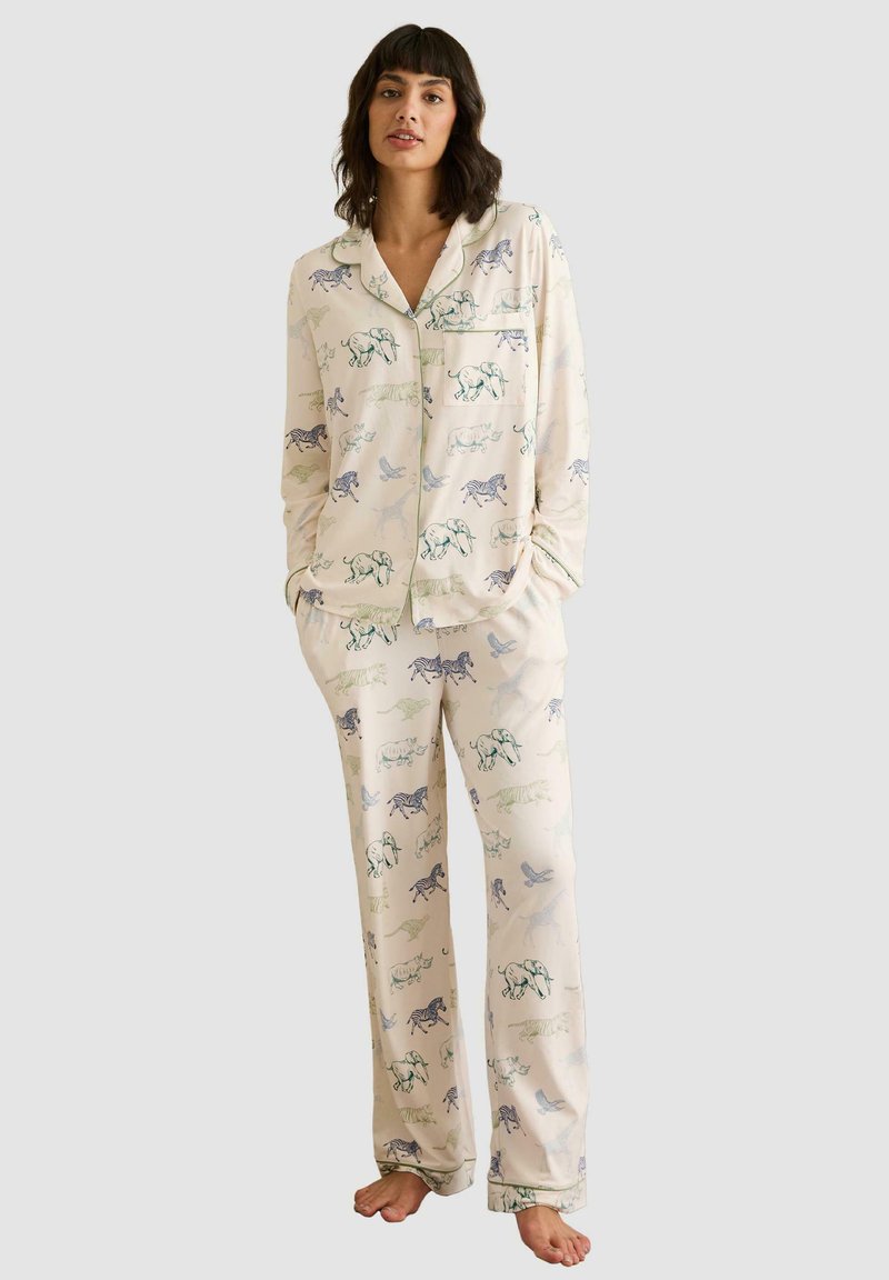 Conjunto de pijama en tejido crema con estampados de animales. Incluye una camisa de botón de manga larga y pantalones a juego con cintura elástica.