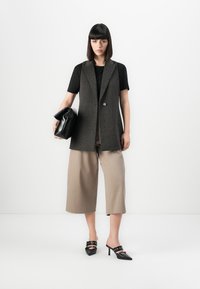 Vesta gri din lână, cu un singur buton, asociată cu un tricou negru, pantaloni largi bej și mules negre cu toc. Poartă un clutch negru în mână.