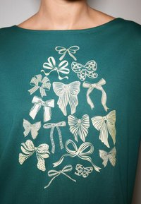 Turkusowa koszulka z różnymi stylizowanymi kokardami w metalicznym złocie. Wzory kokard obejmują solidne, wzorzyste i teksturowane warianty.