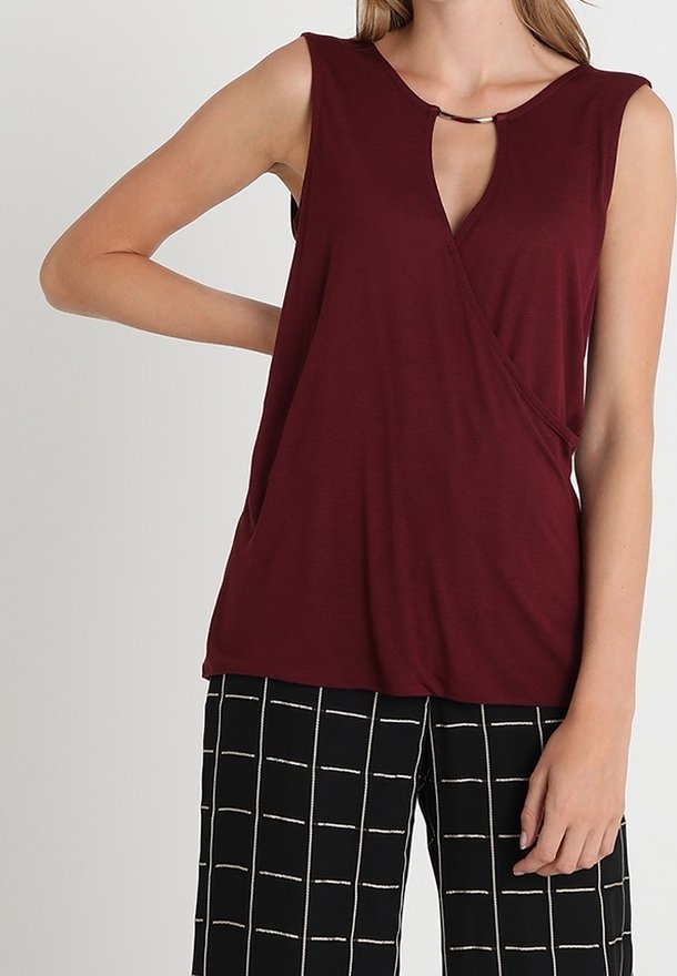 Haut bordeaux sans manches avec encolure goutte d'eau, doté d'un design drapé et d'une texture douce. Associé à un pantalon à carreaux noir et blanc.