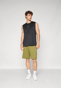 Juoda sportinė be rankovių marškinėliai derinami su alyvuogių žalių trumpikių, abu su minimalistiniu dizainu. Atrodo užbaigia balti sportbačiai.