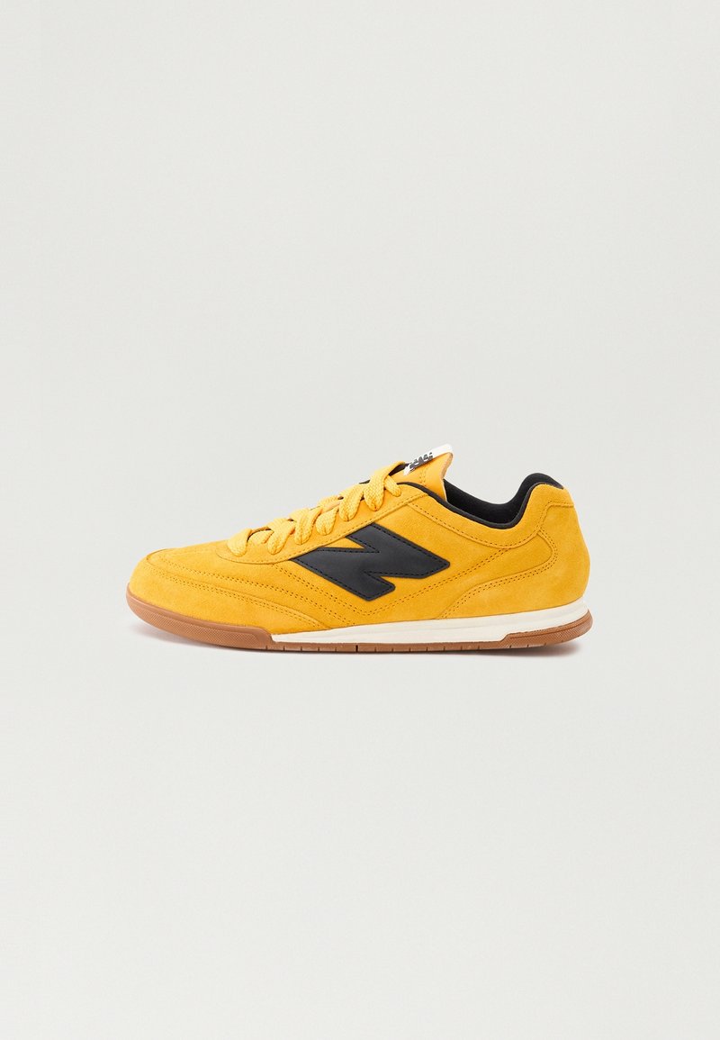 Yellow suede sneaker featuring a black logo, lace-up design, textured upper, and contrasting rubber sole with a gum-colored bottom.