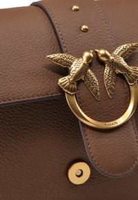 Borsa a tracolla in pelle testurizzata marrone con una chiusura metallica dorata impreziosita da due decorazioni a forma di uccello e un dettaglio a forma di cerchio.