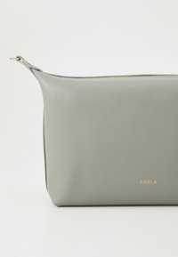 Grön läder kosmetikapåse med dragkedjestängning, rektangulär form, slät textur och guld "FURLA"-logotyp på framsidan.