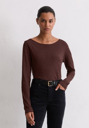 Langärmliges braunes Oberteil aus weichem Stoff mit einem weiten Halsausschnitt. Kombiniert mit schwarzen Hosen und einem schwarzen Gürtel mit einer goldenen Schnalle.