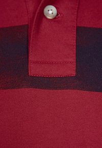 Red polo shirt featuring a dark striped pattern, made of textured fabric with a buttoned collar and a single decorative button.