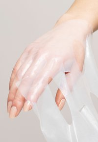 Gennemsigtig, gel-lignende håndmaske der dækker fingre og håndflade, med udskæringer til fingerspidserne og en blank, glat tekstur.