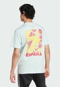 Camiseta de algodón azul claro con un gráfico colorido en la parte posterior, con patrones rojos y amarillos, y la palabra "ESPANA" en negrita roja.
