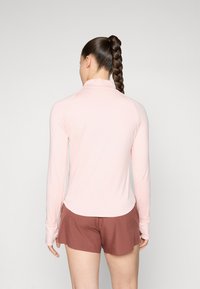 Langermet, lyserosa topp med høy krage, kombinert med brune shortser. Materialet ser glatt ut med tettsittende design og hulrom for tomlene.