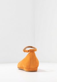 Scarpa piatta in suede arancione, con un design affusolato e cinturino alla caviglia. Superficie texturizzata, tacco basso e soletta liscia per il comfort.