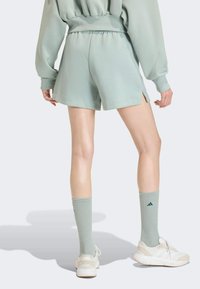 Mint green shorts with side slits, paired with matching knee-high socks and white sneakers featuring a subtle logo. Soft, textured fabric.