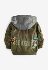 Veste vert olive avec une capuche grise, ornée de patchs et de textes imprimés. Tissu lisse et durable ; poignets et ourlet élastiques pour une coupe ajustée.