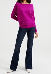 Fuchsia ribbad tröja med bred halsringning, tillsammans med mörkblå utsvängda jeans. Vita skor fulländar outfiten. Enkelt, modernt design.