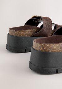 Sandales compensées en daim marron avec semelles épaisses en liège et caoutchouc noir, munies de larges brides et de boucles dorées.