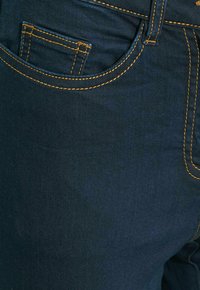 Jeans de denim azul oscuro con costuras naranjas, un bolsillo delantero y una textura suave. El diseño incluye un estilo tradicional de cinco bolsillos.