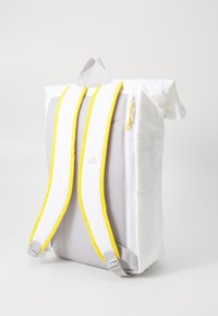 White backpack with grey mesh paneling, yellow straps, and zipper detail. Features a top handle and adjustable, padded shoulder straps.