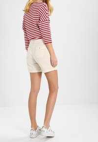 Camisa de manga larga a rayas rojas y blancas combinada con pantalones cortos color crema. Los zapatos tienen patrones de animales sobre un fondo blanco.