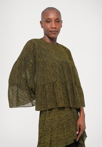 Olivově zelená blůza s paisley vzorem, širokými, volnými rukávy a vrstveným designem, vyrobená z lehkého materiálu.