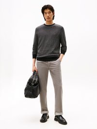 Maglione grigio a maglia con scollo rotondo, pantaloni grigio chiaro slim-fit e scarpe in pelle nere. Il modello tiene una borsa strutturata in pelle nera.