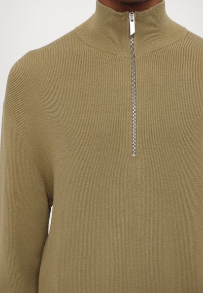 Olive green ribbed knit sweater with a high collar and a silver zipper detail at the front, made from soft, textured fabric.