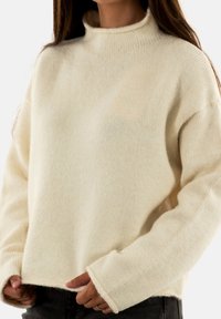 Suéter de punto color crema con cuello alto, corte relajado y mangas largas. Textura suave con detalles de canalé en el cuello y los puños.