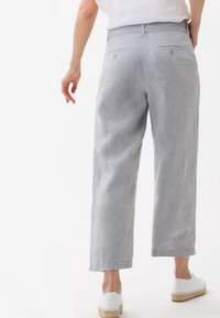 Světlé šedé lněné kalhoty s uvolněným střihem, včetně dvou zadních kapes a nenápadných švů, spárované s bílými espadrilkami.