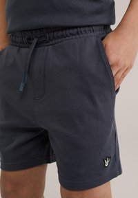 Shorts en coton bleu marine avec une taille élastique, cordon de serrage, poches latérales et un petit logo brodé près de l'ourlet. Texture douce.