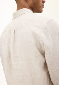 Camicia di lino beige chiaro con colletto alla francese, dettaglio con piega sul retro e finitura in tessuto testurizzato. Progettata per una vestibilità comoda.