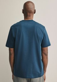Camiseta de manga corta azul marino hecha de algodón suave, con cuello redondo y una textura lisa, vista desde la parte de atrás.